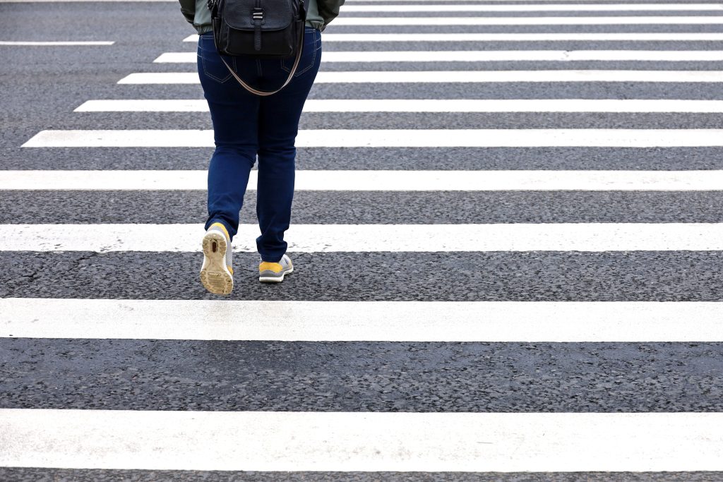 Woman in jeans crossing the street, female legs in sneakers on pedestrian crossing. Concept of road safety